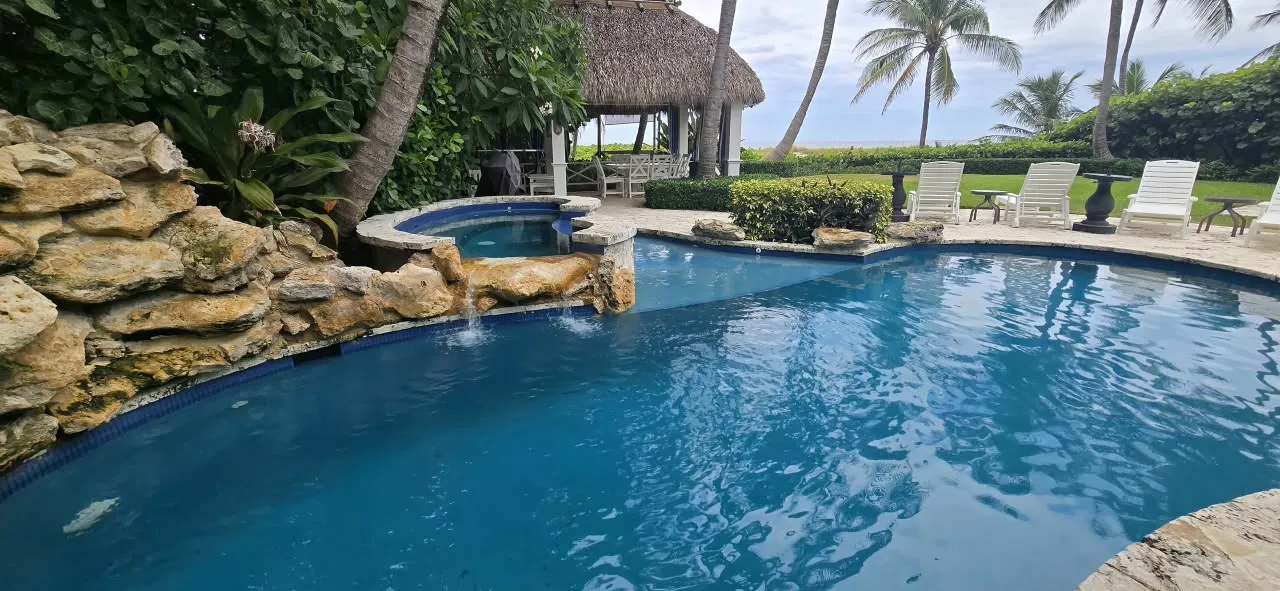 Freeform lagoon pool with a stone waterfall and thatched-roof cabana