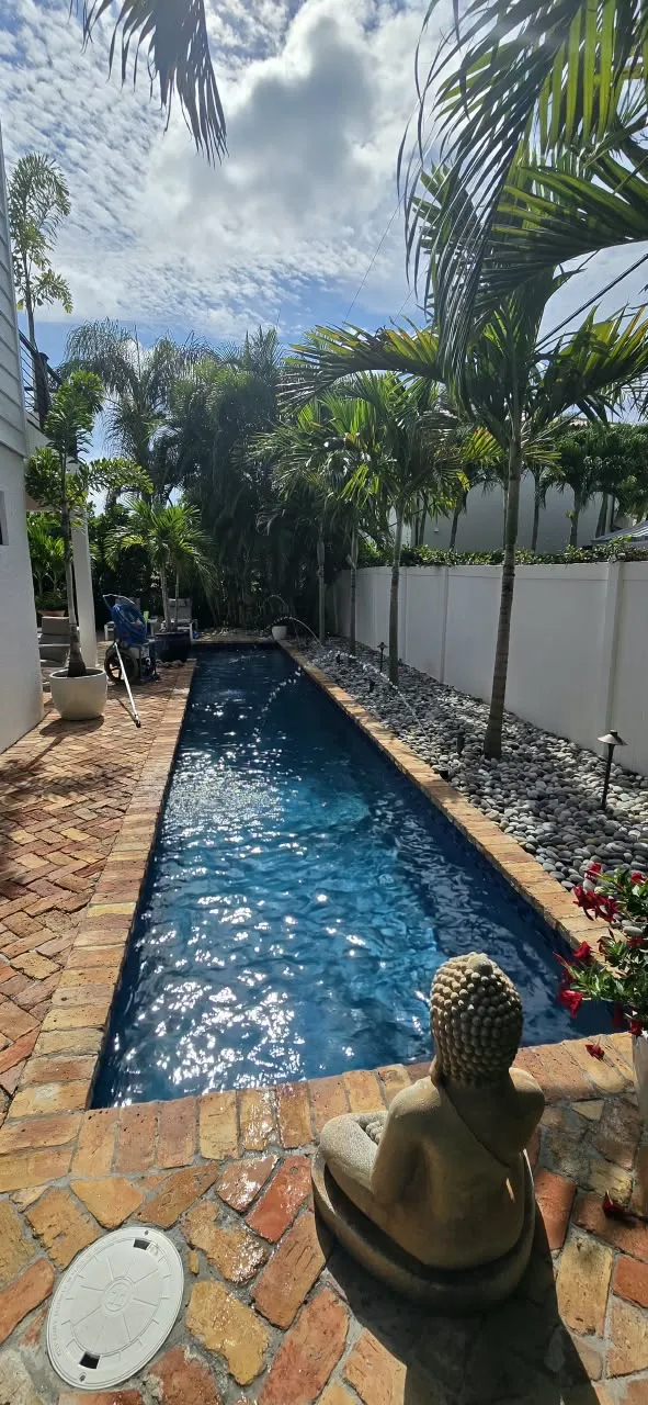 Brick paver walkway beside a narrow lap pool with garden statuary