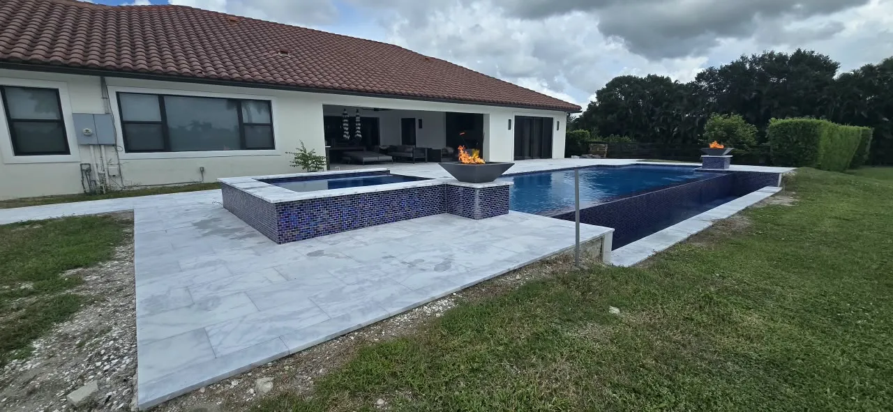 Pool and spa with lit fire bowls on a marble-look paver patio