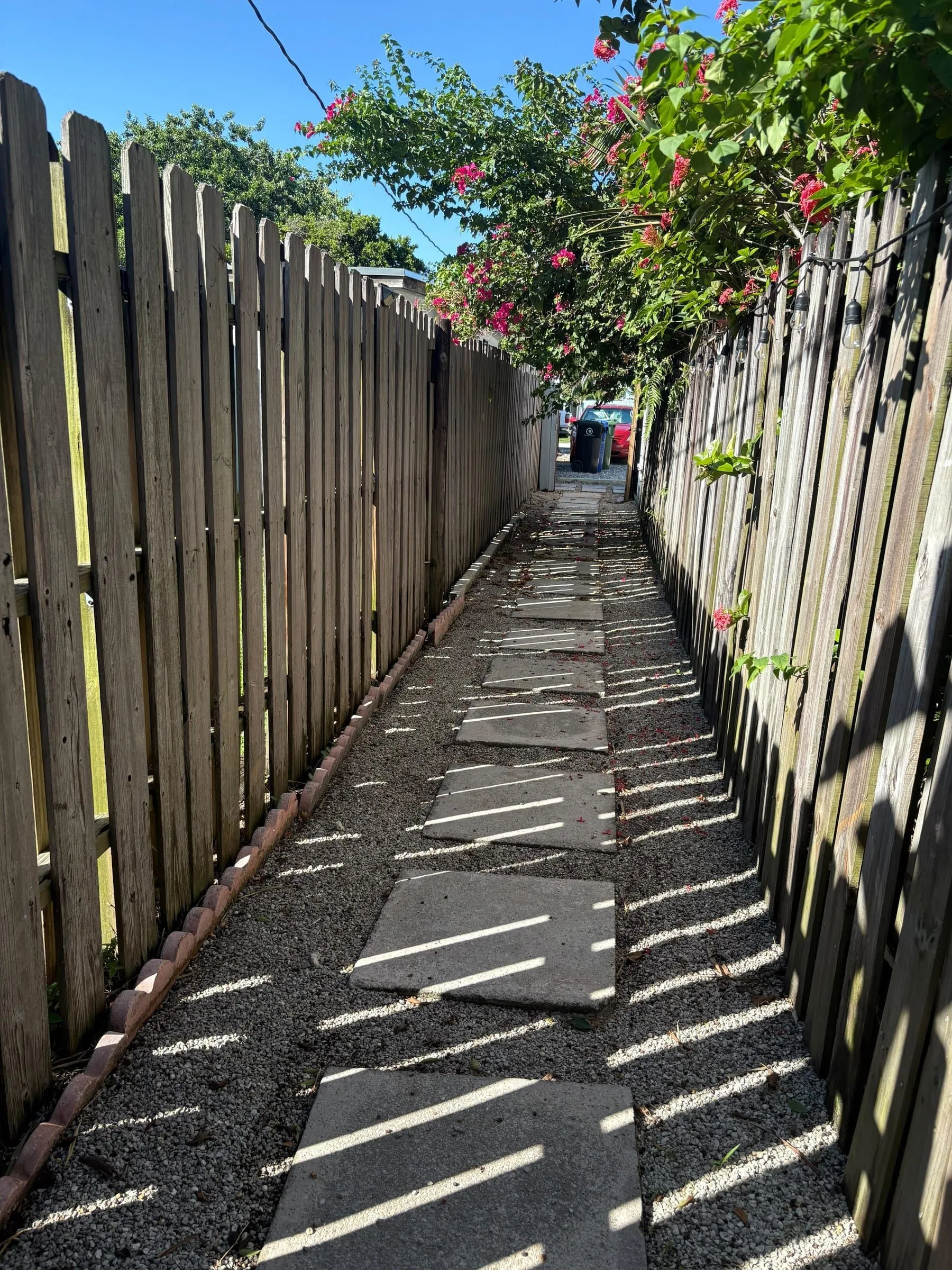 Side yard of loose gravel and concrete stepping stones between two fences
