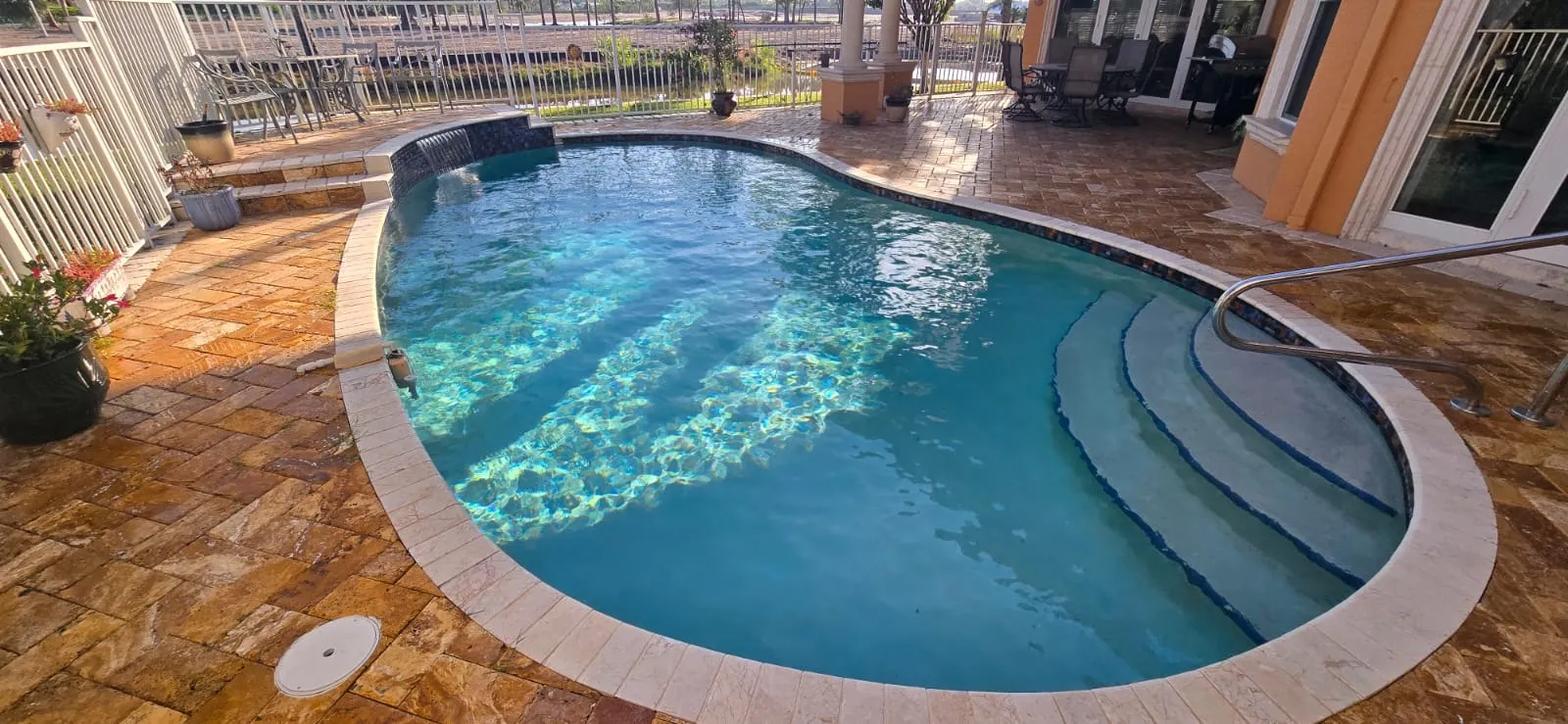 Curved travertine pool deck with paver steps into the water